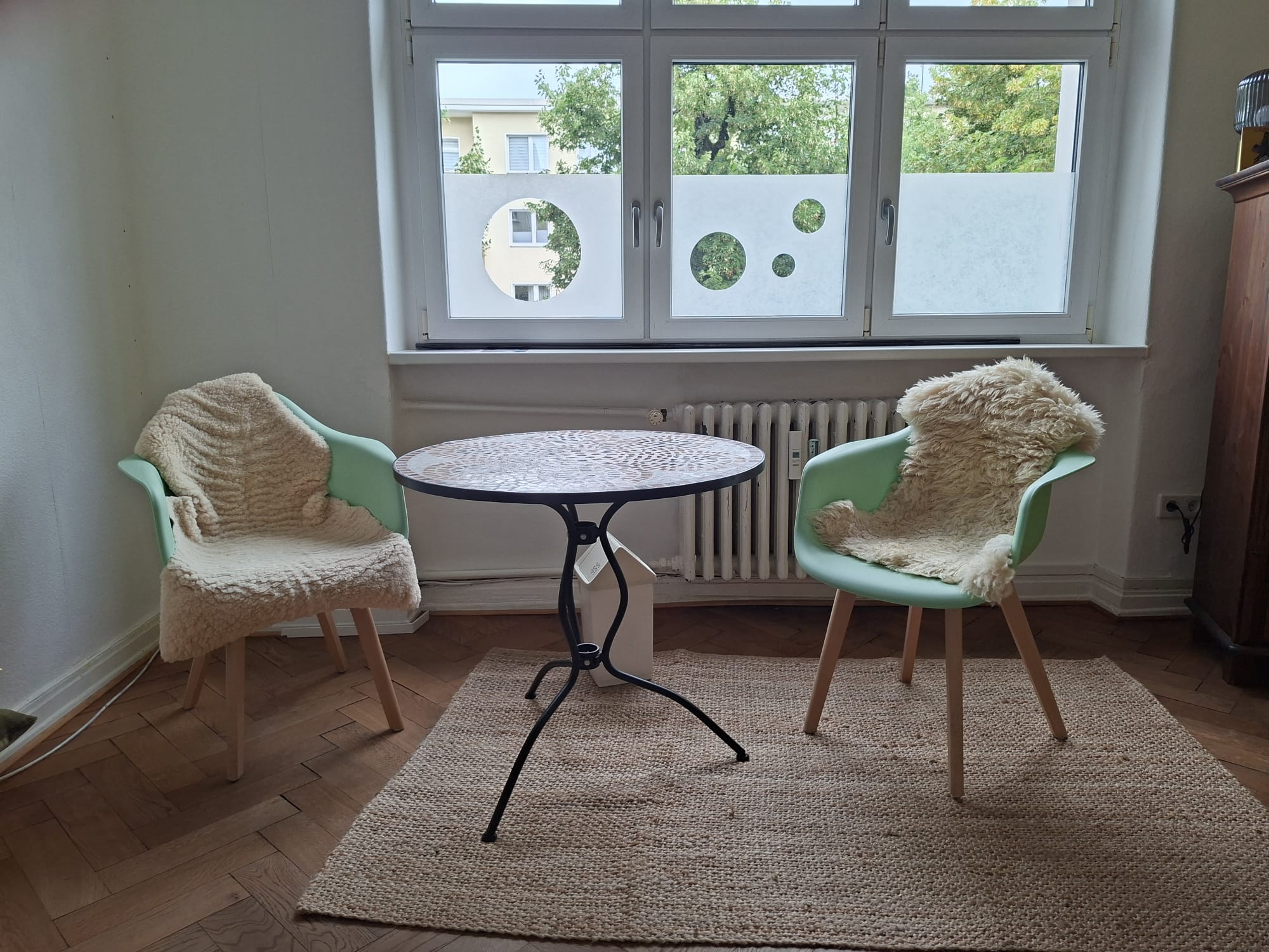Zwei mintgrüne Stühle mit einem runden Tisch vor dem Fenster in Maritas Praxis